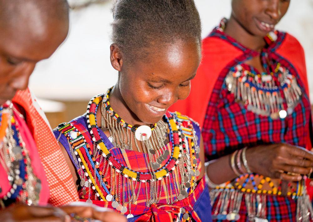 Three Maasai women smiling and beading handicrafts, Masai Mara Kenya.