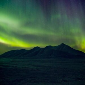 Green northern lights against starry sky over arctic mountains on Basecamp Explorer winter adventure in Spitsbergen.