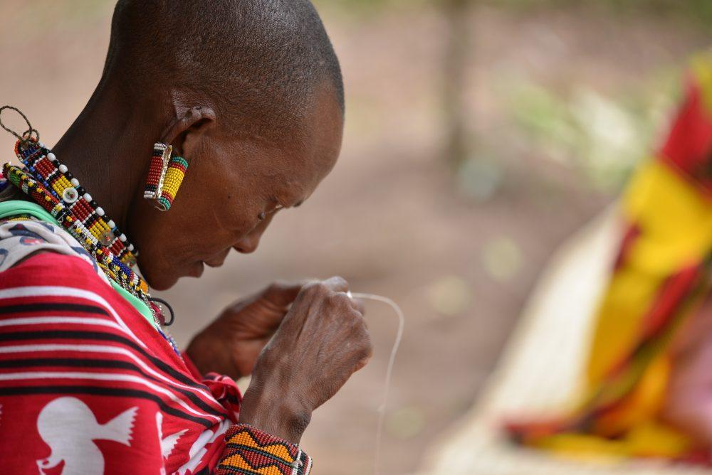 Maasai women in traditional clothes making handicrafts, Kenya.