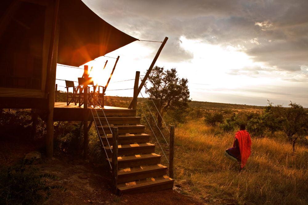 Masai standing outside guest tent looking at sunrise at Eagle View safari camp in Masai Mara.