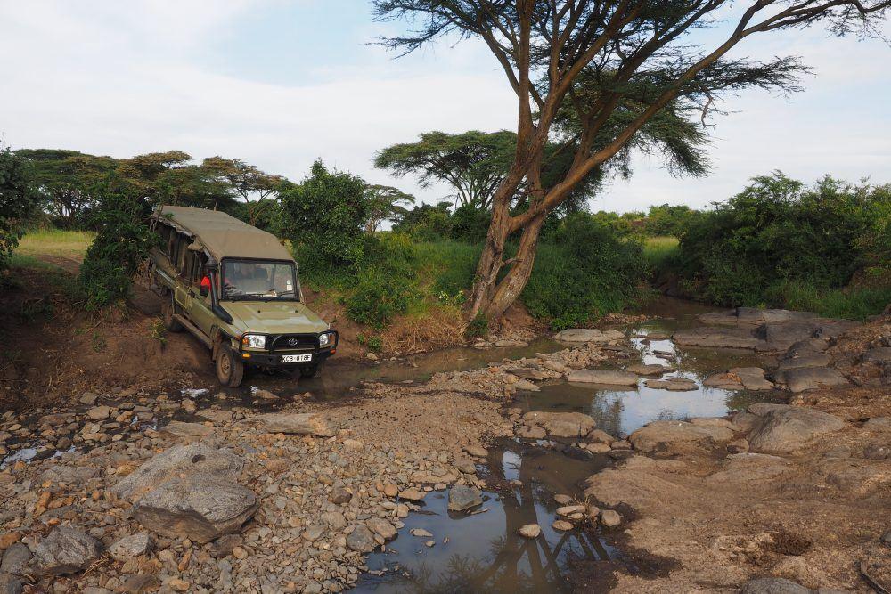 Safari jeep crossing river on a Basecamp Explorer game drive in Masai Mara, Kenya.