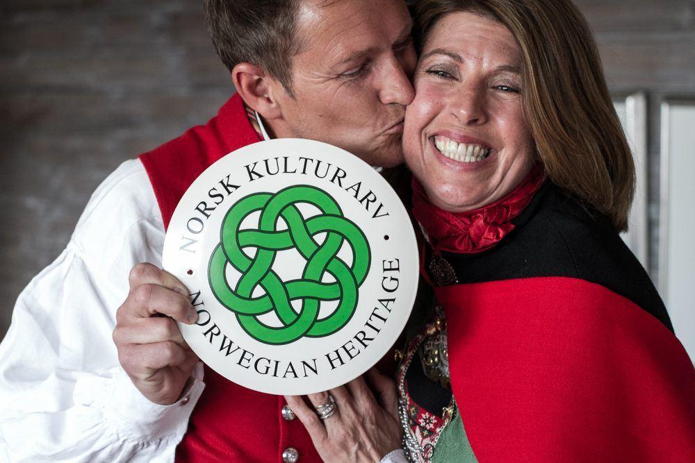 Couple kissing on cheek holding Norwegian heritage sign at Isfjord Radio.