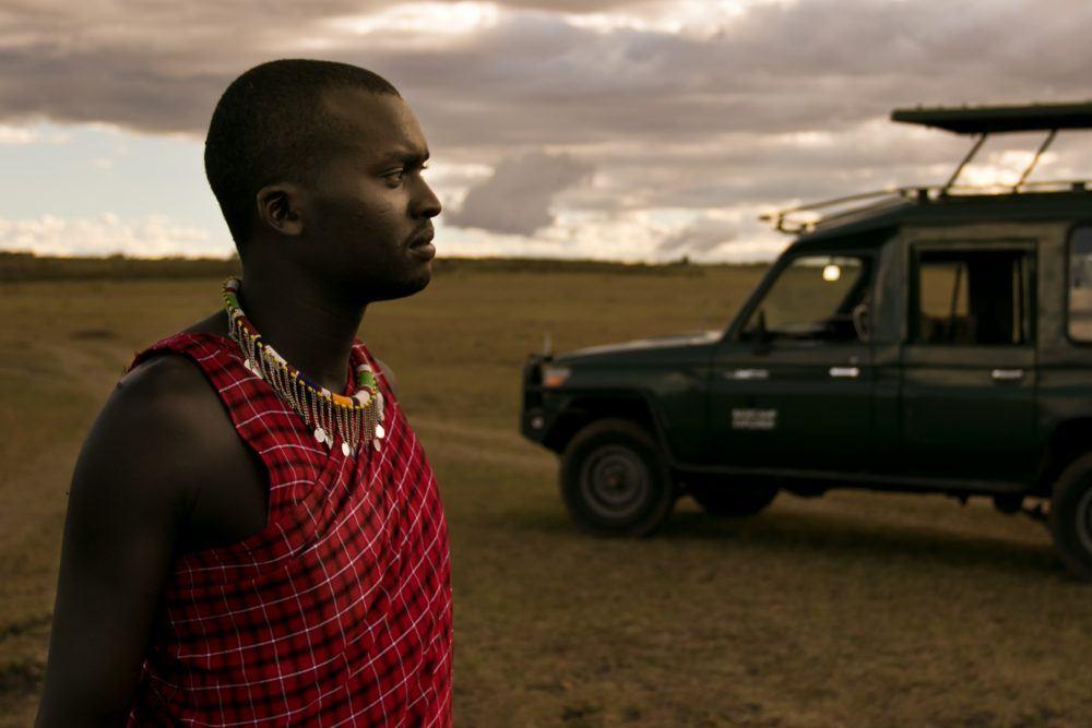 Maasai guide looking into the distance with safari jeep in the background.
