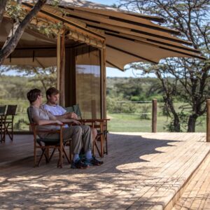 Two men chatting on guest terrace at Basecamp Explorer Leopard Hill safari camp in Mara Naboisho, Kenya.