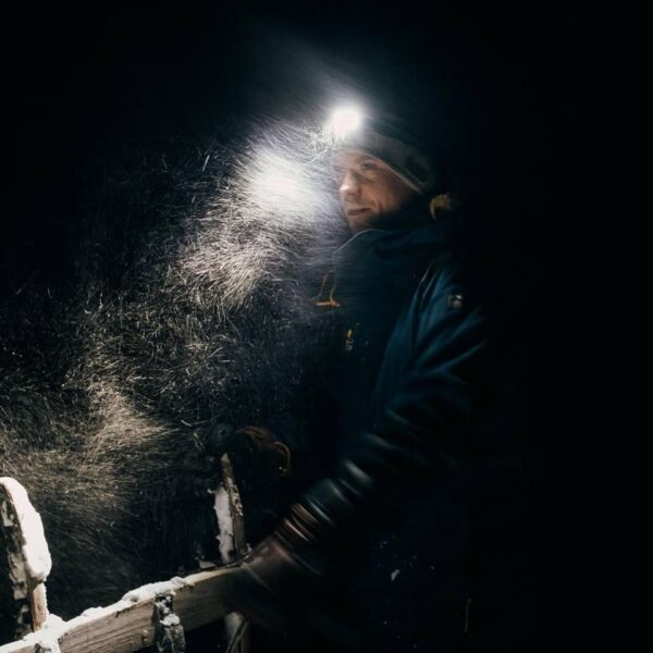 Man dogsledding with headlight in snowstorm on Svalbard.