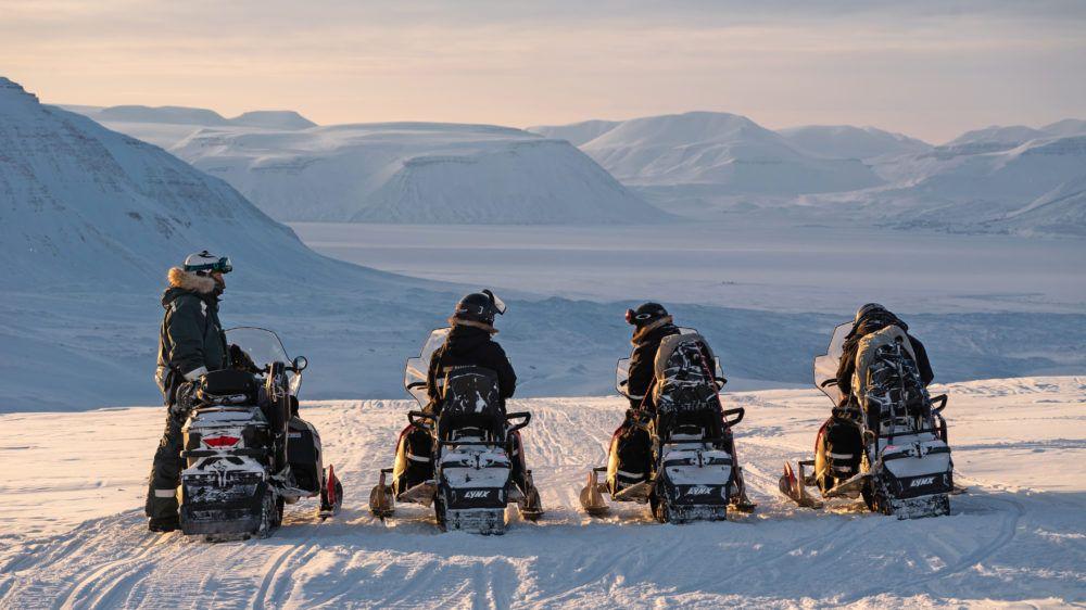 Four people on snowmobiles looking at a large arctic winter valley on a Basecamp Explorer snowmobiling adventure.