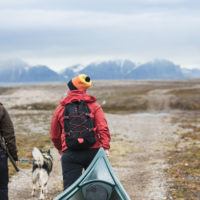 Two women hiking in arctic tundra with husky dog and kayak on Svalbard.